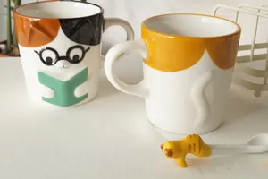 Detail of embossed calico cat ceramic mug with cat-shaped stirring spoon and glasses