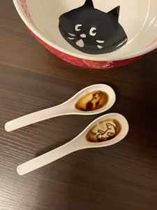 Ceramic soup spoon with embossed cat silhouette detail on a wooden tabletop