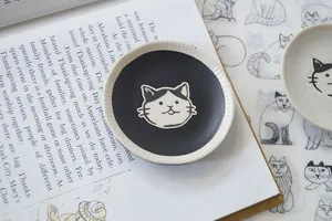 Close-up of a Japanese ceramic sauce dish featuring a hand-painted cat face and ribbed edges