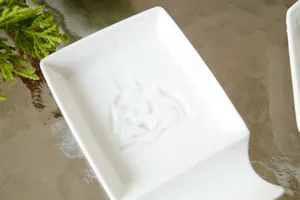 Platillo de cerámica blanca para salsa con relieve de Shiba Inu sobre mesa de madera