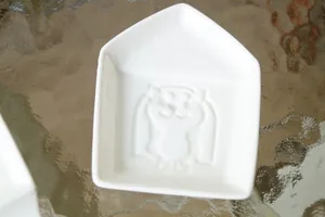 Detalle macro de un plato de cerámica blanca con forma de casa y relieve de gato 3D