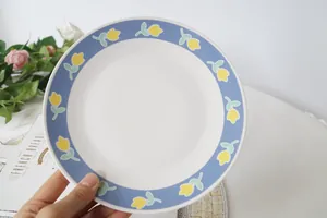 Piatto in ceramica dipinto a mano con tulipani gialli e bordo blu tenuto in mano