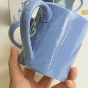Detail of a blue ceramic coffee mug featuring white heart-shaped hand-painted patterns