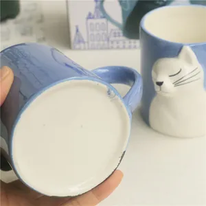Detail of blue ceramic mug base and handle with white 3D cat relief and smooth glaze