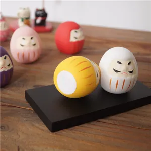 Vue rapprochée de poupées Daruma en céramique colorée sur socle noir et fond bois