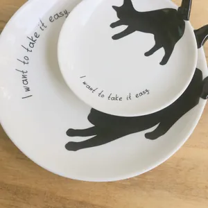 Detalle de platos de cerámica blanca con silueta de gato negro y letras de arte