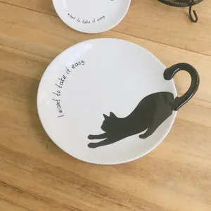 Detalle del plato de cerámica blanca con asa de cola de gato negra y silueta de gatito
