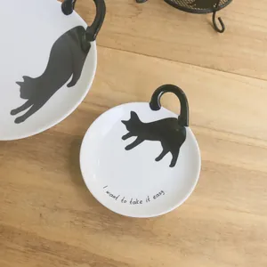 Detalle de platos cerámicos blancos con siluetas de gatos negros y mangos tipo cola