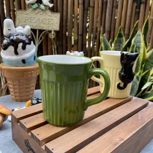 Detail of ceramic cat mugs featuring 3D peeking kitten ornaments and vertical textured stripes