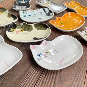 Dettaglio di piattini giapponesi in ceramica a forma di gatto per salse su tavolo di legno