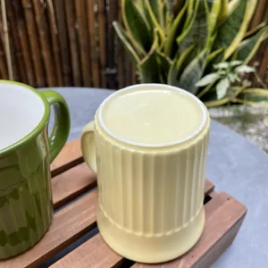 Detailed relief texture on olive green and yellow ceramic mugs atop a wooden tray