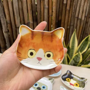 Close-up of cat face ceramic sauce dish with orange patterns and hand for scale