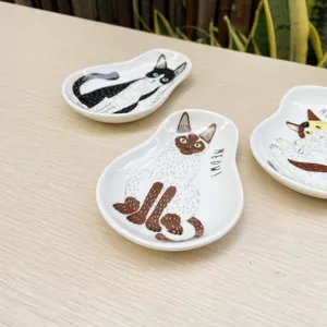 Detailed top view of three ceramic cat sauce dishes on a light wood background