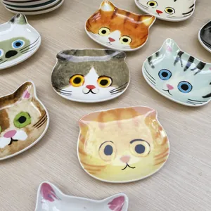 Close-up of cute cat-shaped ceramic sauce dishes in various patterns on wooden table