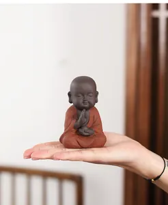 Detail of a miniature purple clay monk tea pet being held in hand to show size