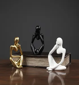 Three abstract thinker statues in gold, black, and white on a vintage book
