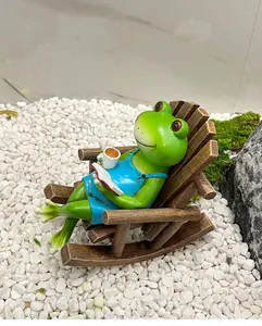 Détail d'une grenouille en résine bleue se relaxant sur une chaise à bascule avec café