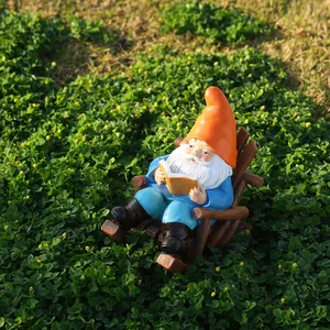Garden gnome statue reading book on wooden rocking chair on green grass lawn