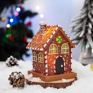 Light-up Christmas gingerbread house resin ornament with warm glowing LED lights and snow detail