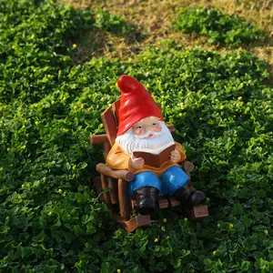 Detail of garden gnome statue sitting on wooden rocking chair reading a book outdoors
