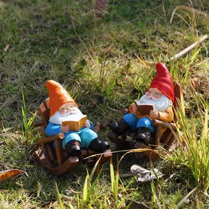 Detailed close-up of two garden gnomes sitting in rocking chairs reading books on grass