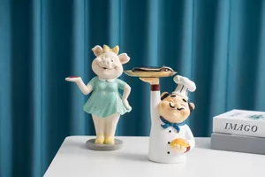 Détail de figurines en résine cochon et chef avec plateau doré sur table blanche