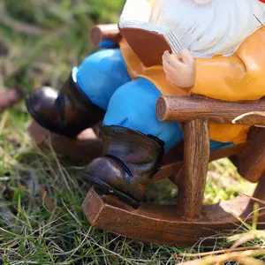Detailed view of garden gnome figurine reading on a wooden rocking chair on green grass