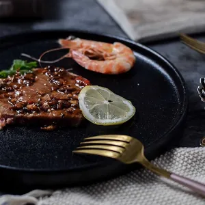 Close-up of matte black ceramic steak plate with grilled beef and gold fork detail