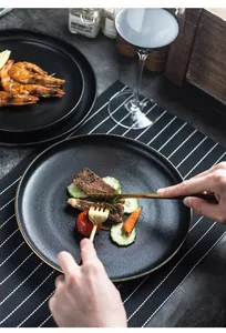 Detail of matte black ceramic steak plate with elegant gold rim and cutlery