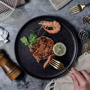 Matte black ceramic round steak plate featuring premium dining setting on stone background