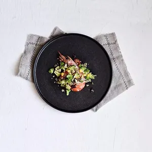 Matte black ceramic dinner plate for steak with prawns and broccoli on a wooden table