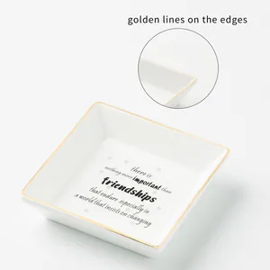Detail of square ceramic jewelry tray featuring gold edges and printed quote inscription
