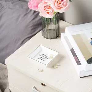 Close-up of square white ceramic jewelry tray with gold rim and inspiring quote print