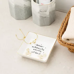 Detail of square ceramic jewelry tray with gold rim, holding heart bracelet and bow earrings