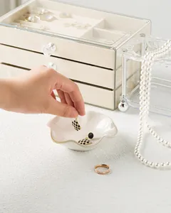 Close-up of clear acrylic jewelry box with beige velvet drawers and ceramic ring tray