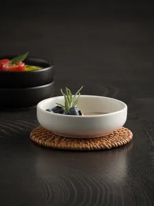 Detail of white ceramic dipping bowl with matte finish on a woven rattan coaster