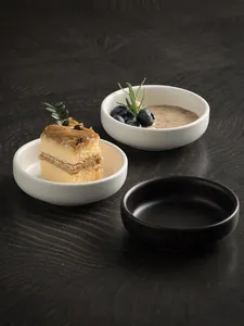Close-up of minimalist ceramic saucer with small cake and sauce on dark wood table