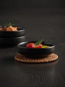 Close-up of matte black ceramic dipping bowl with tomato cubes on a woven mat