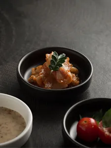 Macro detail of matte black ceramic dipping bowl with kimchi and garnish on dark texture
