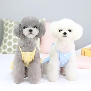 Petits chiens portant des robes d'été en coton jaune et bleu sur un lit blanc moelleux