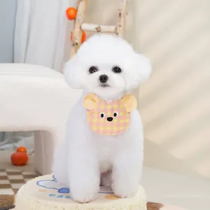 Cute yellow and pink plaid bear-shaped pet bib on a white puppy in a cozy studio setting