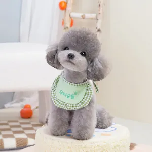 Grey poodle wearing a green checkered pet bib with Korean heart embroidery on a beige stool
