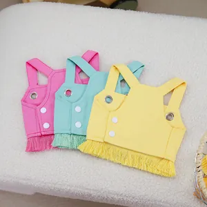 Three colorful pet vests in pink, blue and yellow with fringes on a soft white background