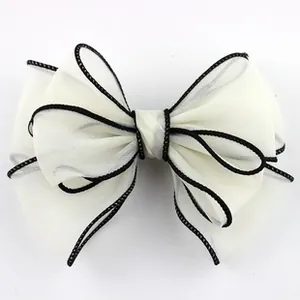 Detail of an ivory organza bow hair accessory with fine black stitched piping edges
