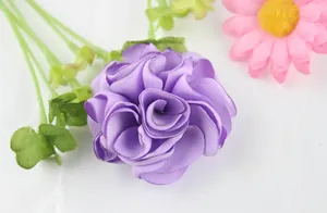 Detail of handcrafted purple ribbon flower brooch with green leaves and realistic petals