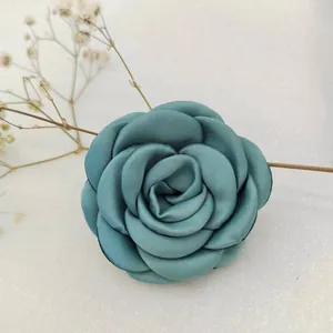 Detail of teal satin fabric camellia flower hair accessory with 3D rolled petals