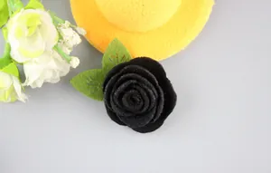 Vista de detalle de un broche de rosa de fieltro negro hecho a mano con hojas verdes