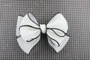 Detail of a white chiffon bow with black stitched edges and double-layer structure
