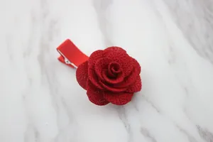 Dettaglio di molletta a rosa in tessuto rosso con trama glitterata su marmo