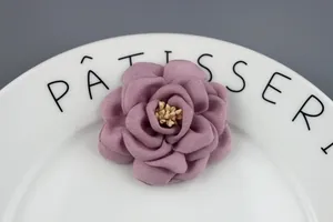 Elegant mauve fabric rose flower hair clip with realistic yellow stamens on a ceramic plate